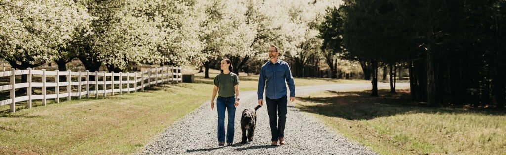 Black dog and 2 owners walking down gravel road